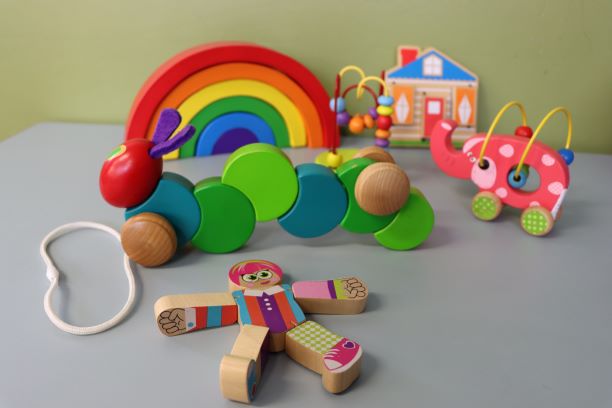 A collection of brightly coloured wooden toys including a pull along caterpillar and a rainbow.